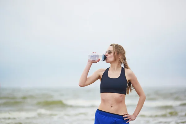 年轻健康的跑步女子在海滩喝水 — 图库照片