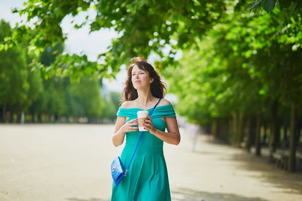 Женщина в зеленом платье ходить с кофе, чтобы пойти в Тюильри сад Парижа, Франция — стоковое фото