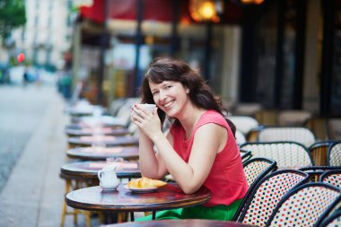 Woman drinking coffee with croissant in Parisian cafe