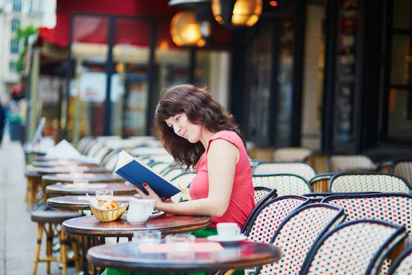 Girl drinking coffee and reading a book in Parisian cafe — Stock Photo, Image