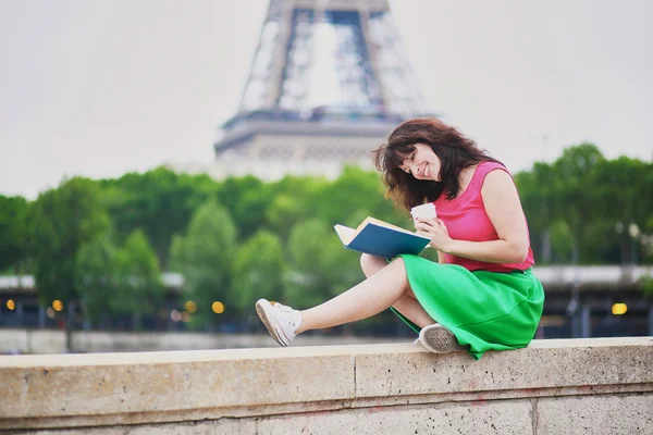 Young girl reading a book near the Eiffel tower — Zdjęcie stockowe