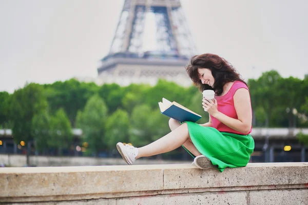 Meisje met koffie te gaan lezen van een boek in de buurt van de Eiffel toren. — Stockfoto