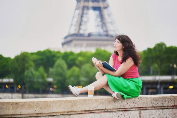 Chica con café para ir a leer un libro cerca de la Torre Eiffel . — Foto de Stock