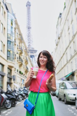 Kahve ve baget ile Paris bir sokakta yürüyen Fransız kadın