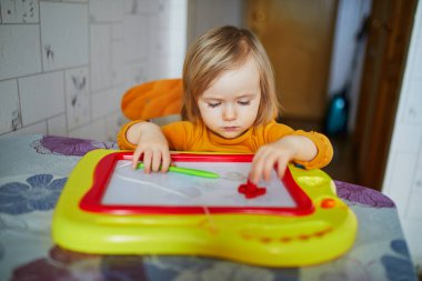 Evde, anaokulunda ya da anaokulunda manyetik büyü ekranına resim çizen sevimli küçük kız. Çocuklar için yaratıcı oyunlar