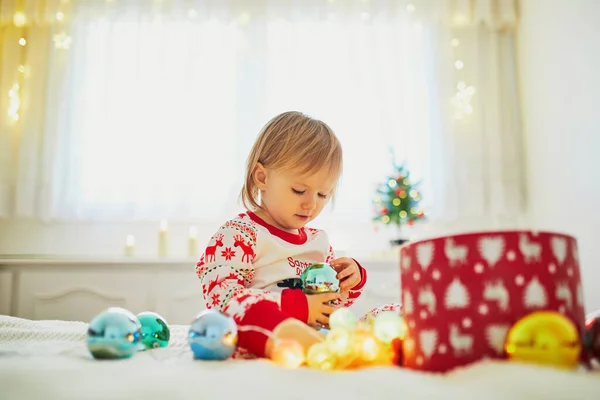 Feliz Niña Pequeña Usando Pijamas Jugando Con Decoraciones Navideñas Cama — Foto de Stock
