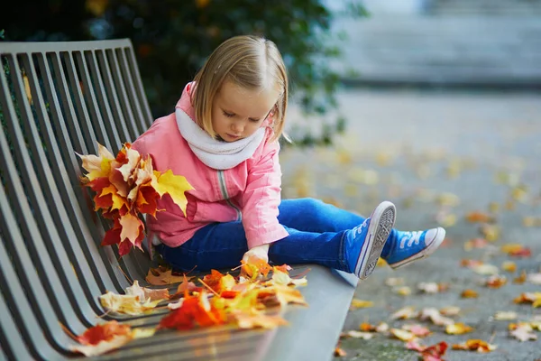 Adorable Niña Sentarse Banco Recoger Las Hojas Caídas Parque Otoño —  Fotos de Stock