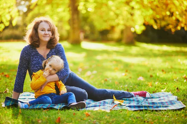 地面に座って秋の公園でピクニックをしている女性と愛らしい幼児の女の子 母と娘は一緒に晴れた秋の日を楽しんでいます 家族のための屋外活動 — ストック写真
