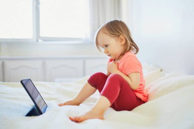 Evde dijital tableti olan küçük bir kız. Çocuk çizgi film izliyor. Çocuk arkadaşlarıyla ya da anaokulu öğrencileriyle iletişim kurmak için alet kullanıyor. Çocuklar için eğitim ve uzak mesafe eğitimi. Evde kalıp eğlenin.