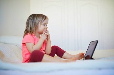 Evde dijital tableti olan küçük bir kız. Çocuk çizgi film izliyor. Çocuk arkadaşlarıyla ya da anaokulu öğrencileriyle iletişim kurmak için alet kullanıyor. Çocuklar için eğitim ve uzak mesafe eğitimi. Evde kalıp eğlenin.