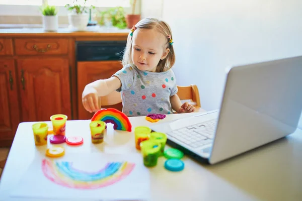 幼児の女の子はラップトップの前でモデリング粘土を再生します 子供はコンピュータを使って友人や幼稚園の生徒とコミュニケーションを取る 子供のための教育やオンライン通信 ホームエンターテイメントに滞在する — ストック写真