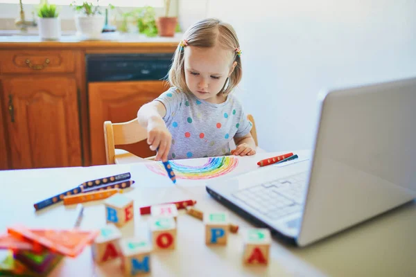 幼児の女の子はノートパソコンの前で虹を描く 子供はコンピュータを使って友人や幼稚園の生徒とコミュニケーションを取る 子供のための教育やオンライン通信 ホームエンターテイメントに滞在する — ストック写真