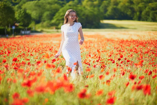 夏の日にケシ畑を歩く白いドレスの美しい若い女性 田舎で花を楽しむ女の子 — ストック写真