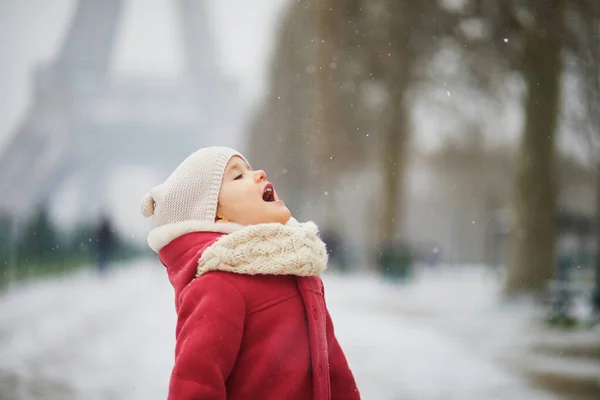 フランス パリのエッフェル塔の近くで舌で雪の結晶をキャッチ愛らしい幼児の女の子 雪と遊ぶ幸せな子供 子供のための冬の活動 — ストック写真