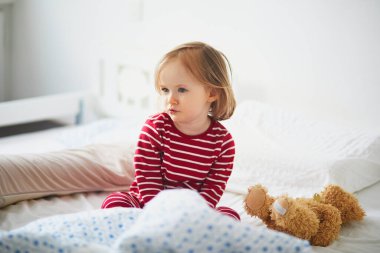 Çizgili kırmızı ve beyaz pijamalı küçük kız uyandıktan hemen sonra yatakta oturuyor. Küçük çocuklar için gündüz şekerlemeleri