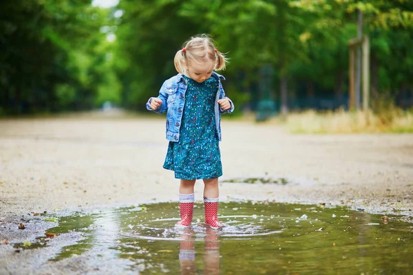 赤いレインブーツを着て夏の日に水たまりに飛び込む子供 雨の日に公園で水と泥で楽しんでいる愛らしい幼児の女の子 子供のための屋外活動 — ストック写真