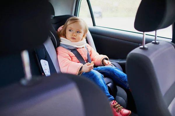 Adorable toddler girl in modern car seat eating cookie. Little kid traveling by car. Child safety on the road. Trip with a baby