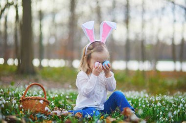 Tavşan kulaklı bir kız Paskalya 'da yumurta avı oynuyor. Bir sürü kartopu çiçeğiyle çimenlerde oturan ve renkli yumurtaları sepette toplayan bir çocuk. Paskalyayı dışarıda kutlayan küçük çocuk.