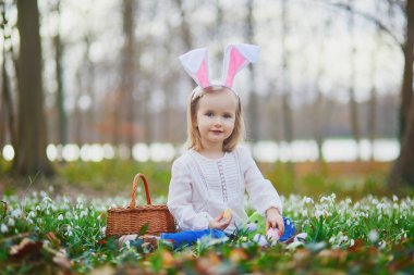 Tavşan kulaklı bir kız Paskalya 'da yumurta avı oynuyor. Bir sürü kartopu çiçeğiyle çimenlerde oturan ve renkli yumurtaları sepette toplayan bir çocuk. Paskalyayı dışarıda kutlayan küçük çocuk.