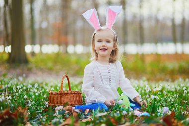 Tavşan kulaklı bir kız Paskalya 'da yumurta avı oynuyor. Bir sürü kartopu çiçeğiyle çimenlerde oturan ve renkli yumurtaları sepette toplayan bir çocuk. Paskalyayı dışarıda kutlayan küçük çocuk.