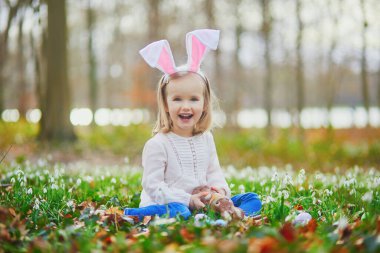 Tavşan kulaklı bir kız Paskalya 'da yumurta avı oynuyor. Bir sürü kartopu çiçeğiyle çimenlerde oturan ve çikolatalı tavşan yiyen bir çocuk. Paskalyayı parkta ya da ormanda kutlayan küçük bir çocuk.