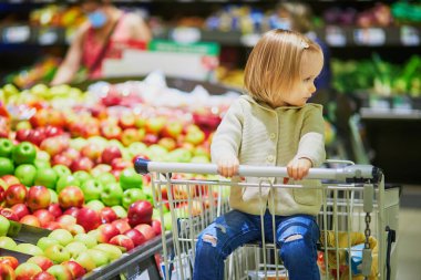 Markette ya da süpermarkette alışveriş arabasında oturan küçük tatlı bir kız. Küçük çocuk alışverişe gidiyor. Çocuklar için sağlıklı yiyecekler