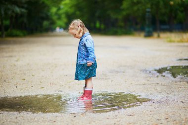Kırmızı çizme giyen ve yaz günü su birikintisine atlayan bir çocuk. Tatlı küçük kız yağmurlu bir günde parkta su ve çamurla eğleniyor. Çocuklar için açık hava aktiviteleri