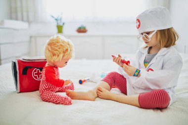 Beyaz önlüklü, şırıngayla doktorculuk oynayan ve bebeğine tıbbi bakım yapan sevimli bir kız. Çocuklar ve rol oyunları. Covid-19 aşı kavramı