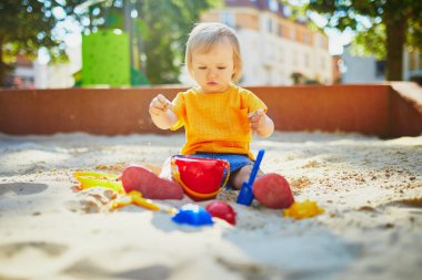 Sevimli küçük kız kum havuzunda oyun parkında eğleniyor. Bebek kum kalıplarıyla oynuyor ve çamur yapıyor. Çocuklar için açık hava yaratıcı aktiviteler
