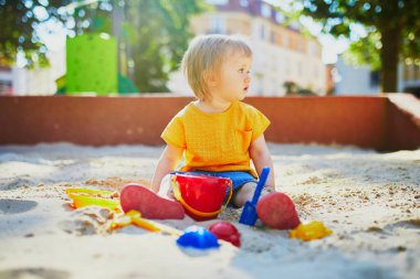 Sevimli küçük kız kum havuzunda oyun parkında eğleniyor. Bebek kum kalıplarıyla oynuyor ve çamur yapıyor. Çocuklar için açık hava yaratıcı aktiviteler