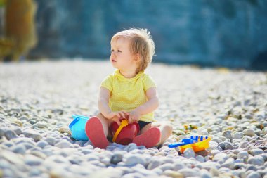 Sevimli küçük kız sahilde çakıl taşlarıyla oynuyor. Küçük çocuk Etretat, Normandiya, Fransa 'da deniz kenarında eğleniyor. Çocuklar için açık hava aktiviteleri