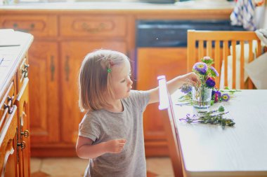 Sevimli küçük kız evde çiçek buketi yapıyor. Çocuk suya aster koyuyor. Çocuklar için ev aktiviteleri