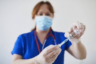 Steteskoplu kadın doktor ya da hemşire, yüz maskesi ve steril eldiven takıyor, elinde şırınga ve COVID-19 aşısı tutuyor. Araştırma, klinik deney, aşı ya da sürü dokunulmazlığı konsepti