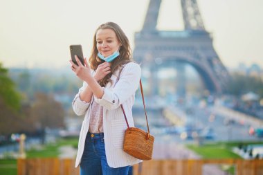 Coronavirus salgını sırasında yarı yarıya çıkarılmış yüz maskesi takmış, selfie çeken ya da video blogu kaydeden bir kız. Fransa 'da salgın ve tecrit. Fransa 'da turist tatili