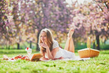 Güzel genç bir kadın güneşli bahar gününde parkta piknik yapıyor kiraz çiçeği mevsiminde