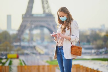 Paris 'teki Eyfel Kulesi yakınlarında koruyucu yüz maskesi takan ve koronavirüs salgını sırasında dezenfektan kullanan bir kız. Fransa 'da salgın ve tecrit. Salgın sırasında Fransa 'da turist tatili