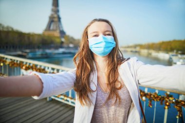 Paris 'te Eyfel Kulesi yakınlarında maske takan ve selfie çeken ya da Coronavirus salgını sırasında video blogu kaydeden bir kız. Fransa 'da salgın ve tecrit. Salgın sırasında Fransa 'da turist tatili
