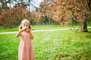 Pembe elbiseli sevimli bir kız güneşli bahar gününün tadını çıkarıyor ve Fransa, Paris yakınlarındaki Sceaux Park 'ta ahşap fotoğraf makinesiyle oynuyor.