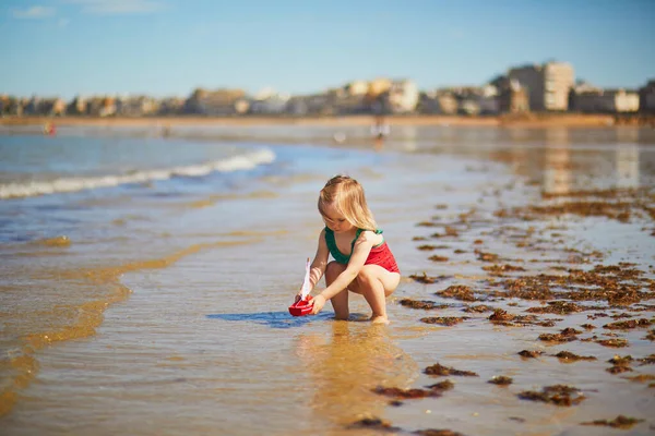Очаровательная Девочка Красном Купальнике Играет Деревянной Игрушечной Лодкой Воде Пляже — стоковое фото