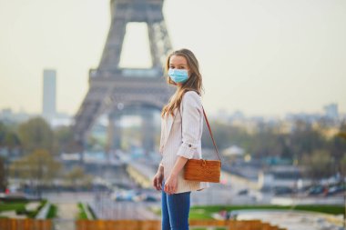 Paris 'teki Eyfel Kulesi' nin yanında duran ve Coronavirus salgını sırasında koruyucu maske takan genç bir kız. Fransa 'da salgın ve tecrit. Salgın sırasında Fransa 'da turist tatili