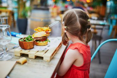 Üç yaşında güzel bir kız kafede ya da restoranda hamburger yiyor. Çocuk konseptiyle çıkmak