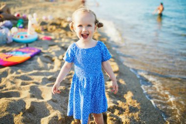 Mavi elbiseli mutlu küçük kız Fransa 'nın Akdeniz sahilinde eğleniyor. Neşeli çocuk denizde tatilin tadını çıkarıyor. Çocuklar için açık hava yaz etkinlikleri