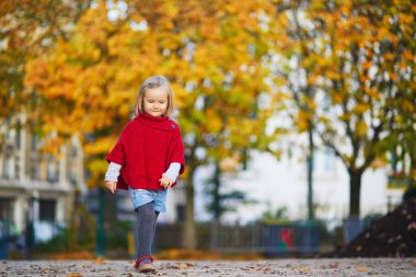 Sonbahar parkında güneşli bir sonbahar gününde kırmızı pançolu sevimli küçük kız yürüyor. Mutlu çocuk Paris, Fransa 'nın bir caddesinde eğleniyor. Çocuklar için açık hava sonbahar aktiviteleri