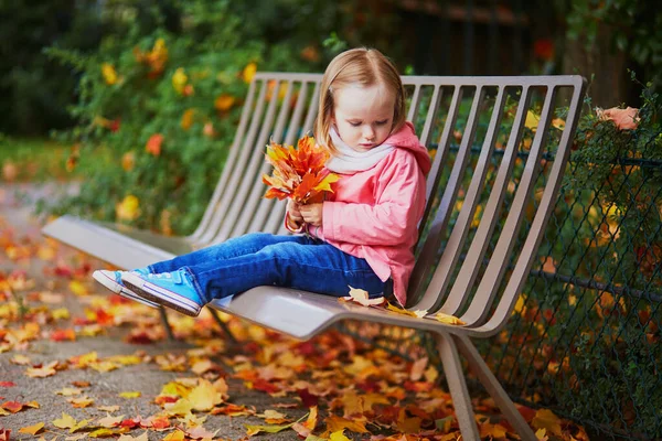 ベンチに座って秋の公園に落ちた葉を集める愛らしい幼児の女の子 フランスで秋の日を楽しんで幸せな子供 子供のための屋外活動 — ストック写真