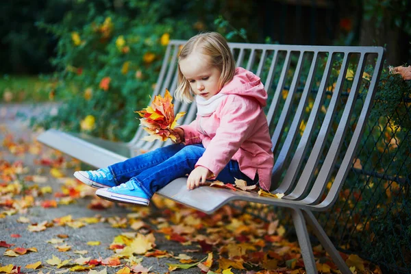 Αξιολάτρευτο Κοριτσάκι Που Κάθεται Στον Πάγκο Και Μαζεύει Πεσμένα Φύλλα — Φωτογραφία Αρχείου