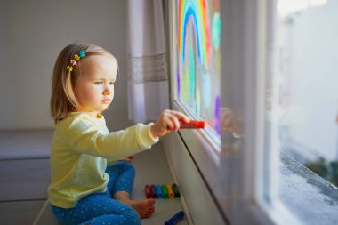 Pencere camına gökkuşağı çizen sevimli küçük kız. Yaratıcı oyunlar ve evdeki çocuklar için aktiviteler. Yaratıcılık ve hayal gücü geliştirme kavramı