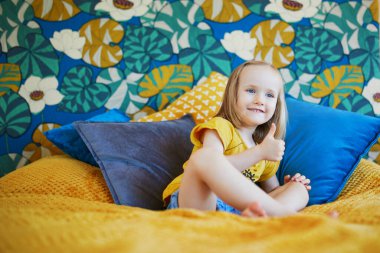 Güzel dekore edilmiş yatak odasında, yatakta oturan sevimli, oynak küçük kız.