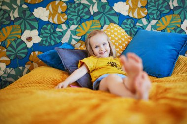 Güzel dekore edilmiş yatak odasında, yatakta oturan sevimli, oynak küçük kız.