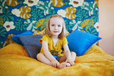 Güzel dekore edilmiş yatak odasında, yatakta oturan sevimli, oynak küçük kız.