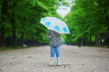 Sonbahar günü şemsiyeli yağmurluk giyen bir çocuk. Tatlı küçük kız yağmurlu bir günde eğleniyor. Çocuklar için açık hava sonbahar aktiviteleri